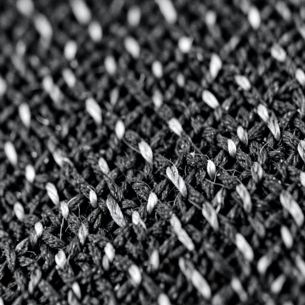 Dark monochrome close-up of woven material with deep crevices and pale ridges forming a repeating textile pattern